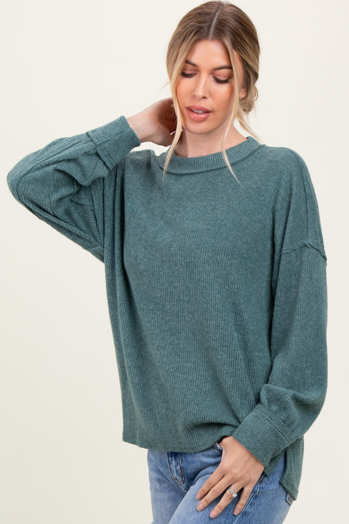 woman wearing a green ribbed oversized sweater and blue jeans, posing with one hand on her neck