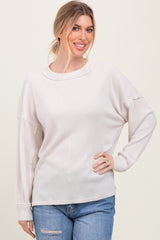 woman wearing a light beige oversized ribbed sweater with a wide neckline and distressed sleeve detail paired with blue jeans