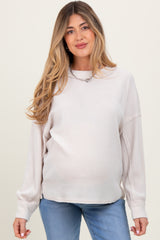 woman wearing a light beige maternity sweater with long sleeves and a relaxed fit, showing her baby bump