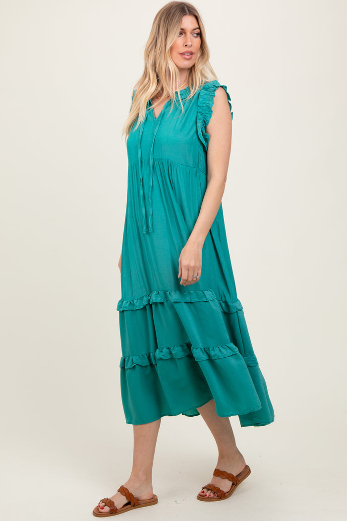 woman wearing a teal maxi dress with ruffle details and tie neck, standing against a plain background