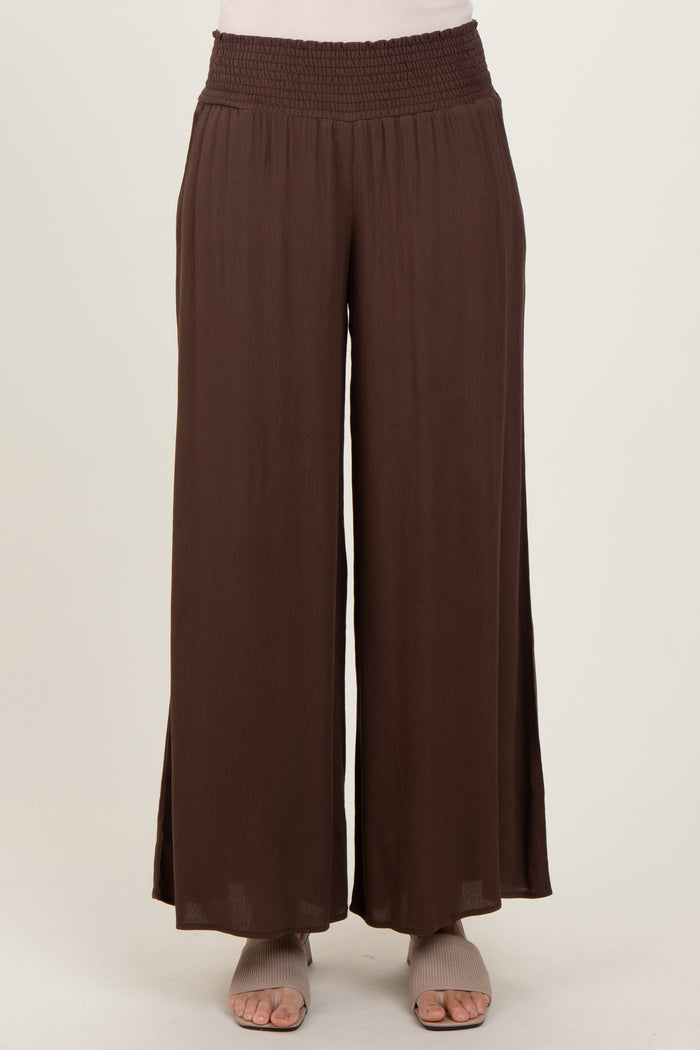 woman wearing brown wide-leg pants with a smocked waistband and side slits, styled with open-toe shoes