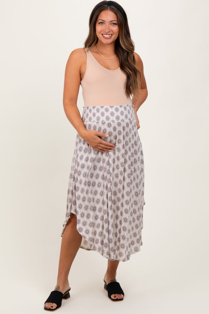 woman wearing a beige maternity dress with a printed skirt and holding her baby bump