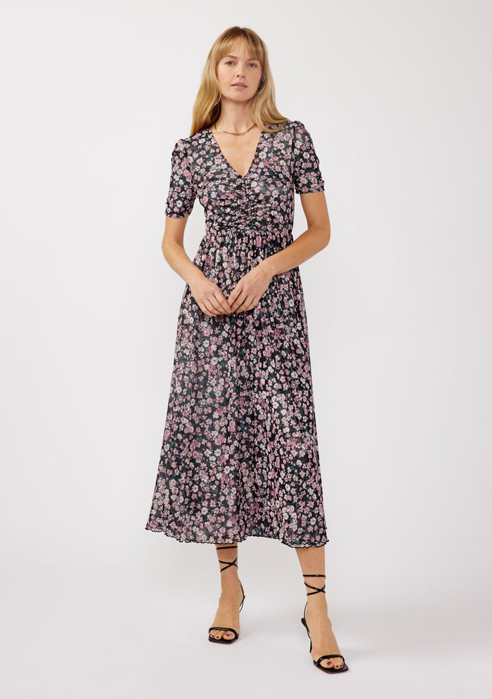 woman wearing a black floral maxi dress with short sleeves and a wrap design, standing against a white background