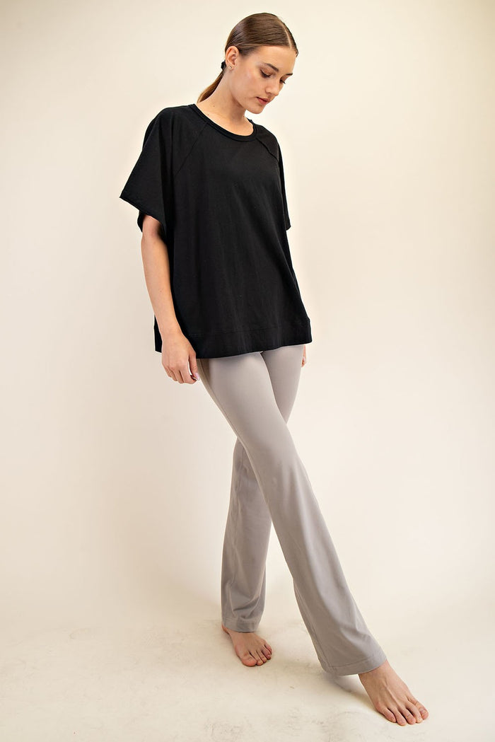 woman wearing a black oversized t-shirt and light gray flared pants, standing barefoot against a neutral background