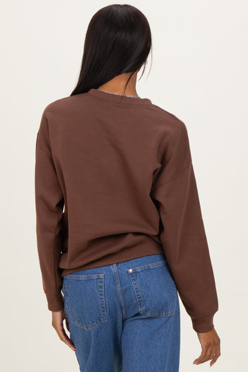 woman wearing a brown oversized sweatshirt with a relaxed fit and blue high-waisted jeans, viewed from the back