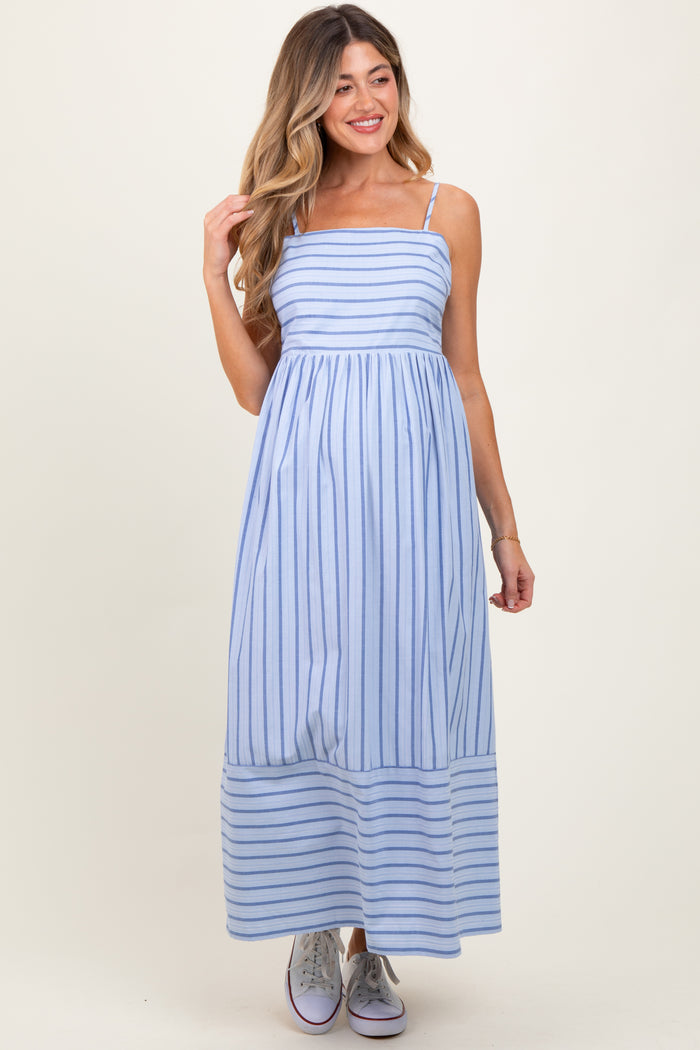 woman wearing a light blue striped maternity maxi dress with thin straps and a flowing skirt, holding her hair