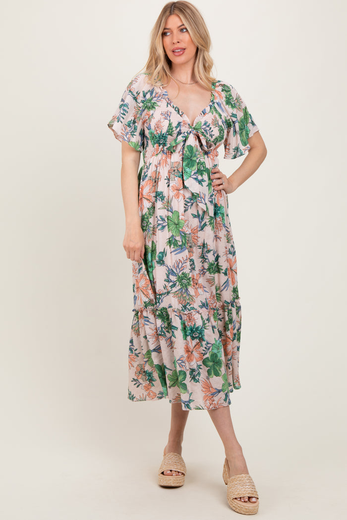 woman wearing a floral print maxi dress with short flutter sleeves and a tie front detail in a light pastel color