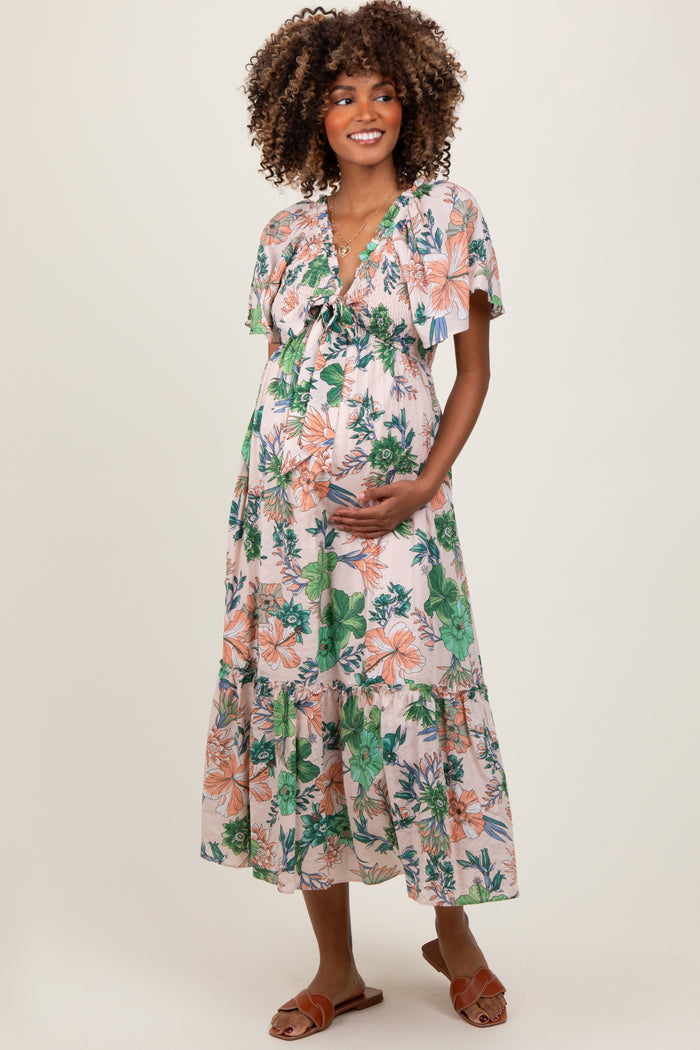 woman wearing a floral maternity maxi dress with short sleeves and a flowing skirt, holding her baby bump