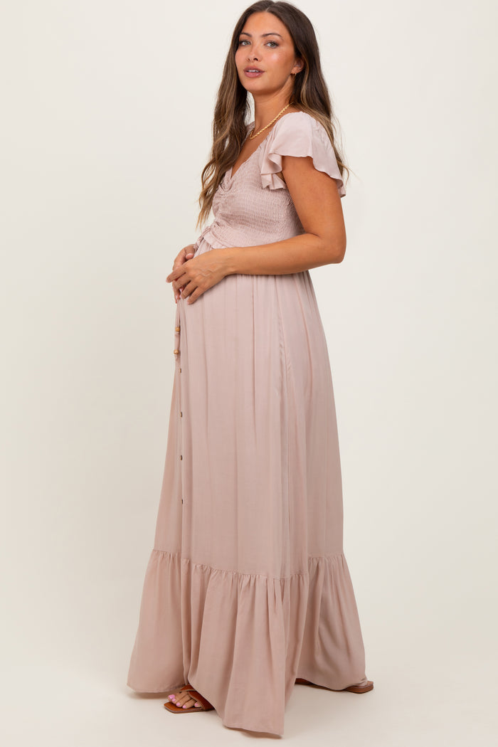 woman wearing a blush pink maternity maxi dress with ruffle sleeves and a fitted bodice, showing her baby bump