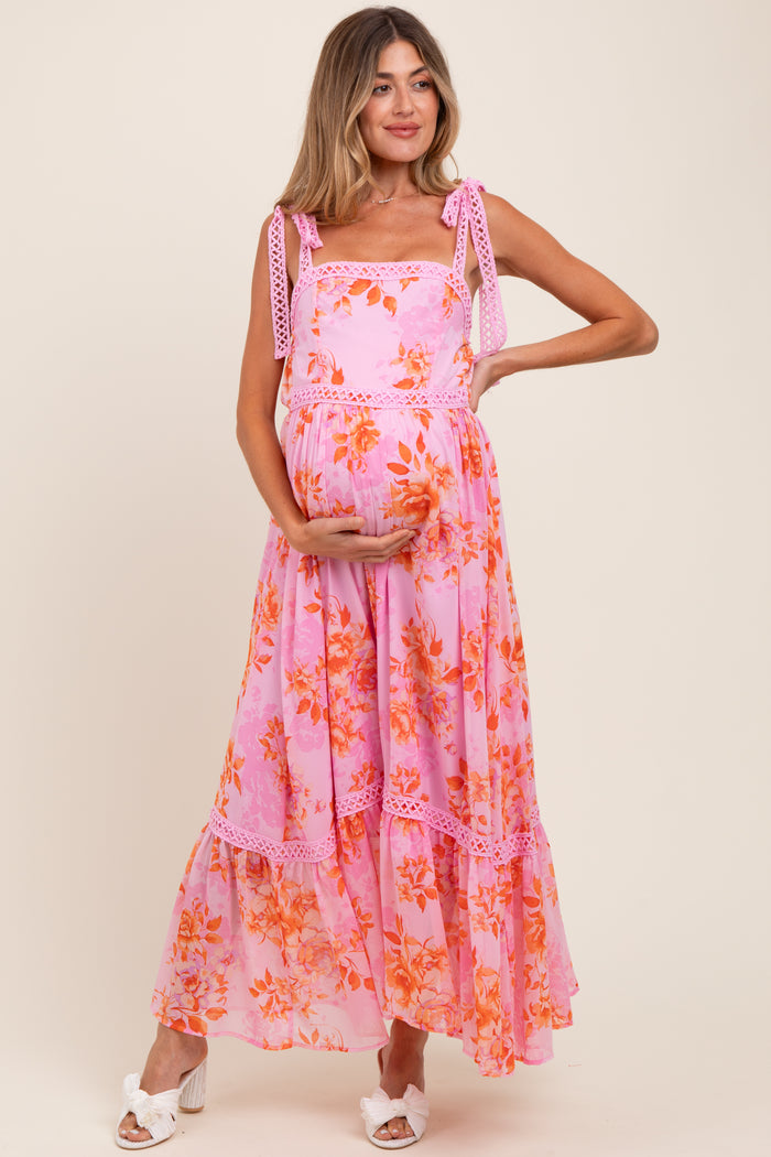 woman wearing a pink floral maternity maxi dress with tie straps and holding her baby bump
