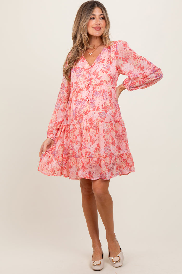 woman wearing a pink floral maternity dress with long sleeves and a tiered design, showcasing a baby bump