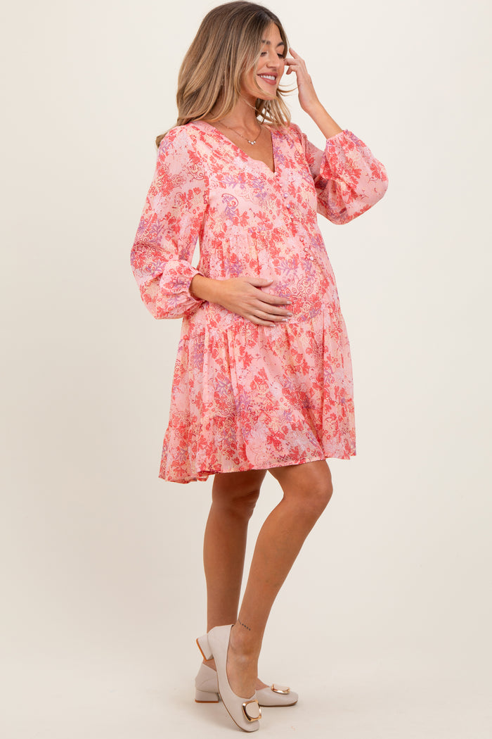 woman wearing a pink floral maternity dress with a v-neck and puff sleeves, holding her baby bump