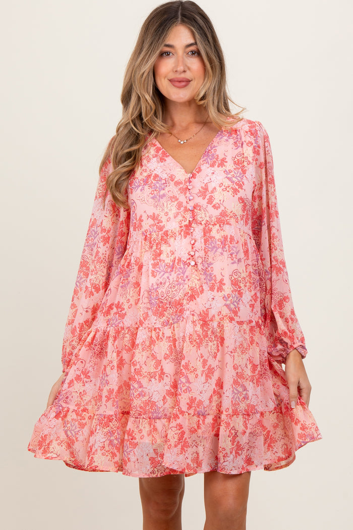 woman wearing a pink floral maternity dress with long sleeves and a tiered skirt, smiling at the camera