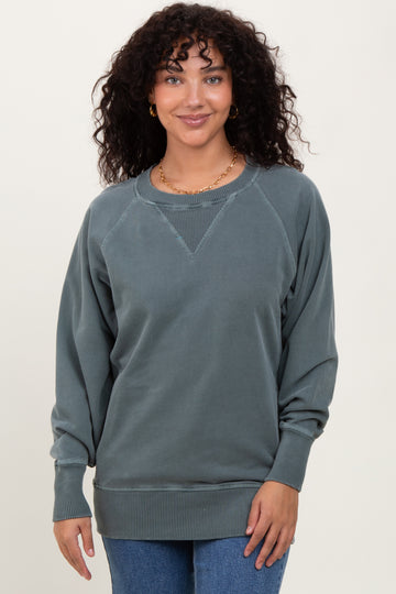 woman wearing a dark teal oversized sweatshirt with a scoop neckline and ribbed hem, smiling at the camera