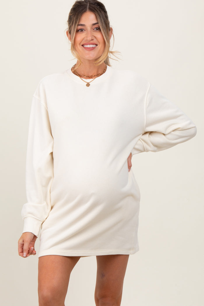 woman wearing a cream long sleeve maternity dress with a visible baby bump and smiling at the camera