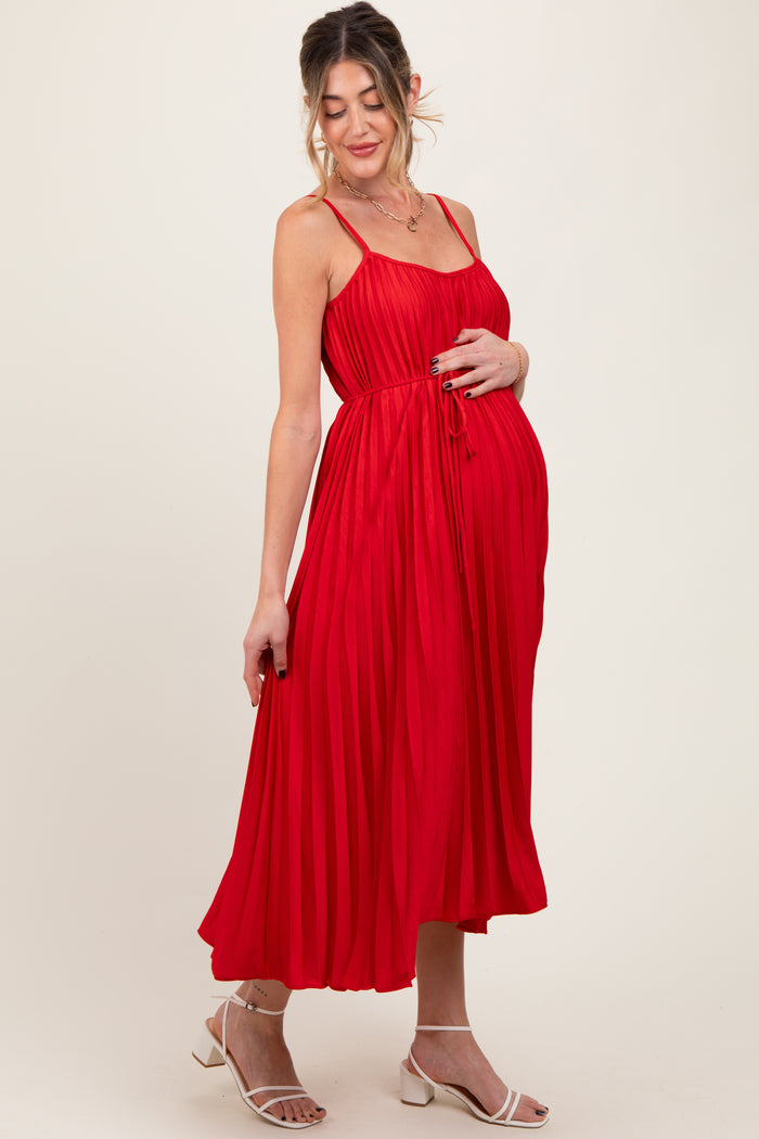 woman wearing a red pleated maternity dress and holding her baby bump