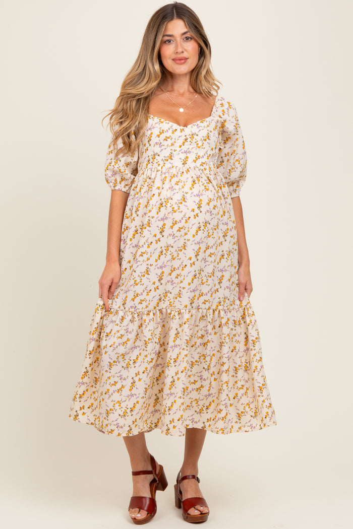 woman wearing a floral maternity dress with puffed sleeves and a tiered skirt, showcasing her baby bump