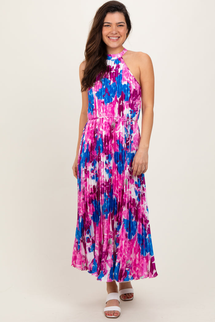 woman wearing a halter neck pleated maxi dress in pink and blue floral print with a fitted bodice and flowy skirt