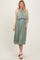 woman wearing a sage green pleated halter neck midi dress with a layered top and white heeled sandals