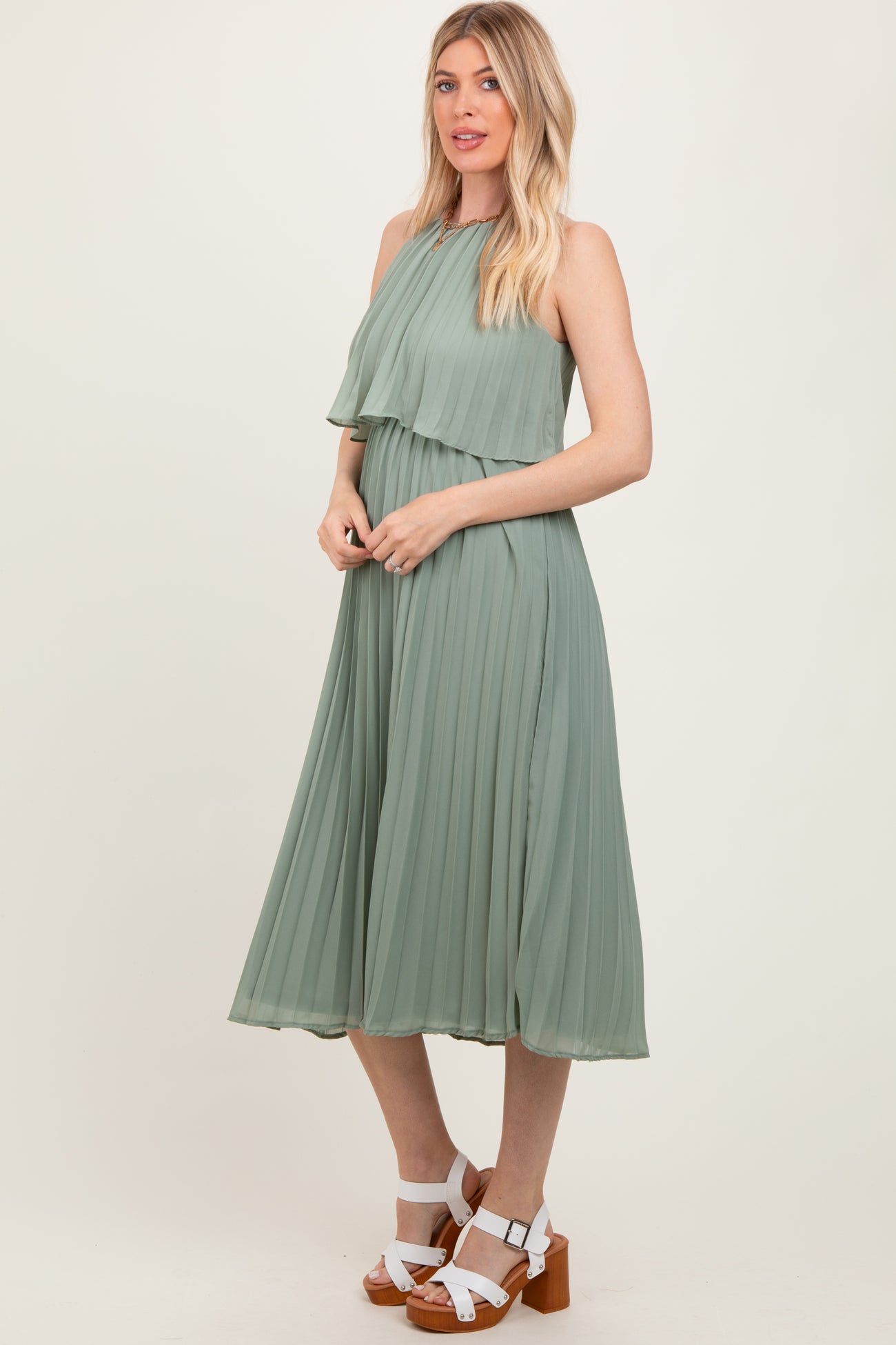 woman wearing a green pleated midi dress with layered detailing and standing in a relaxed pose