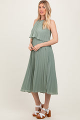 woman wearing a green pleated midi dress with layered detailing and standing in a relaxed pose