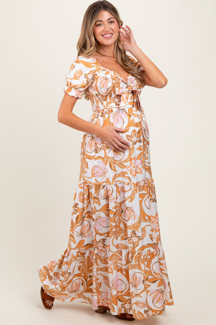 woman wearing a floral maternity maxi dress with puff sleeves and a baby bump, smiling and posing with one hand on her hip
