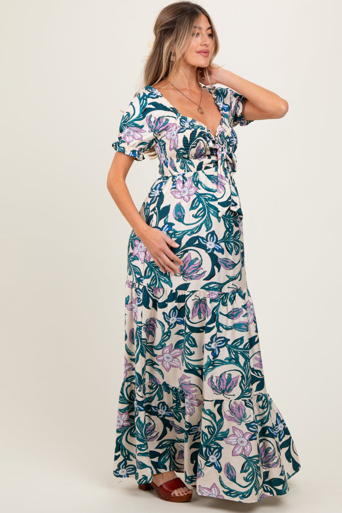 woman wearing a floral maternity maxi dress with a fitted bodice and ruffled sleeves, cradling her baby bump