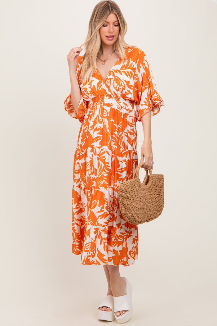 woman wearing an orange and white floral midi dress with puff sleeves, holding a straw bag and wearing platform sandals