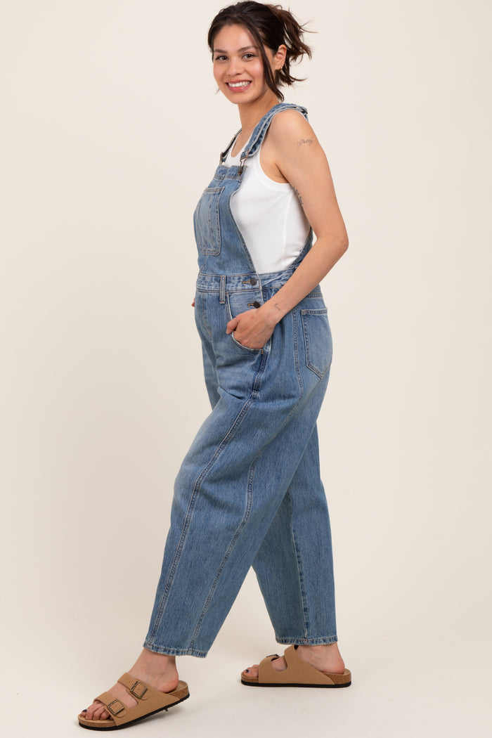 woman wearing maternity denim overalls with a white tank top and brown sandals, no visible baby bump