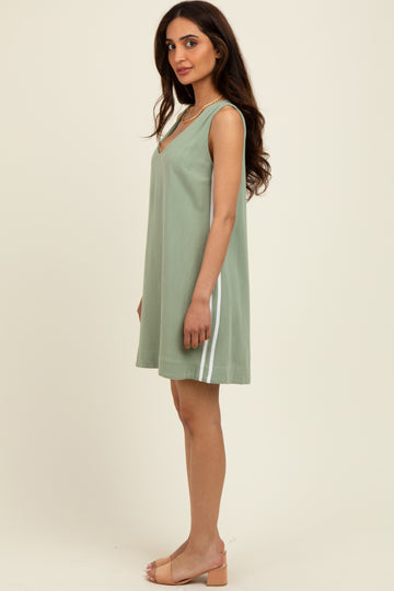 woman wearing a green sleeveless shift dress with white side stripes and sandals, standing sideways against a light background