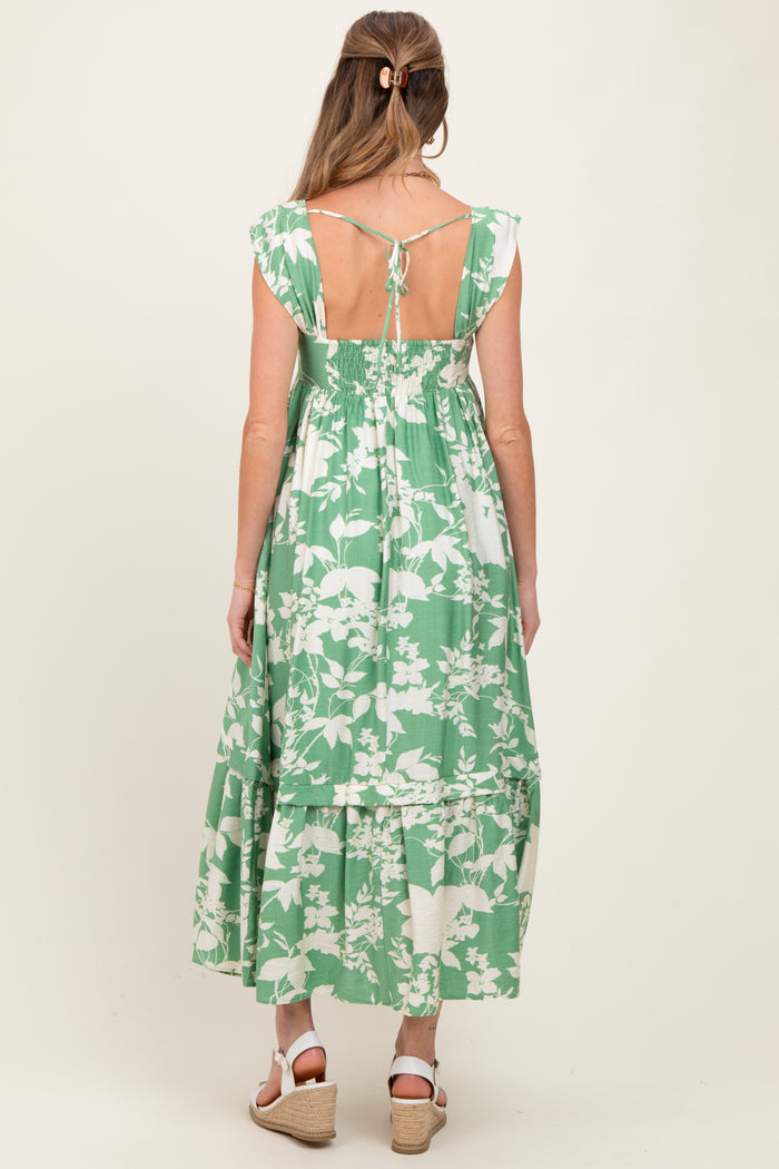 woman wearing a green floral maternity maxi dress with a tie back and ruffled hem