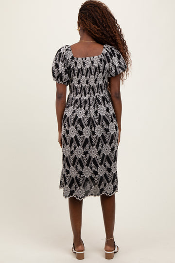 woman wearing a black floral embroidered midi dress with puff sleeves and a square back design