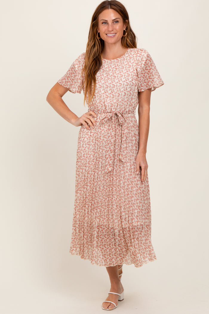 woman wearing a pink floral maxi dress with short sleeves and a tie belt, standing and smiling at the camera