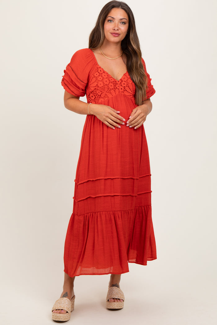 woman wearing a red tiered maternity dress with puff sleeves and lace detailing, gently holding her baby bump