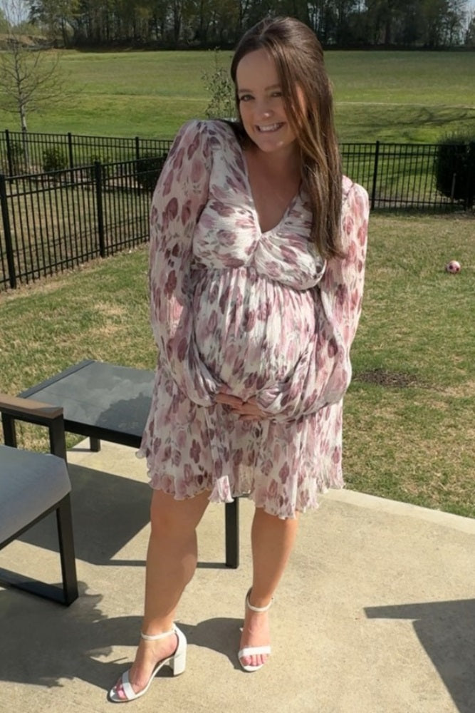 woman wearing a floral print maternity dress with long sleeves and holding her baby bump