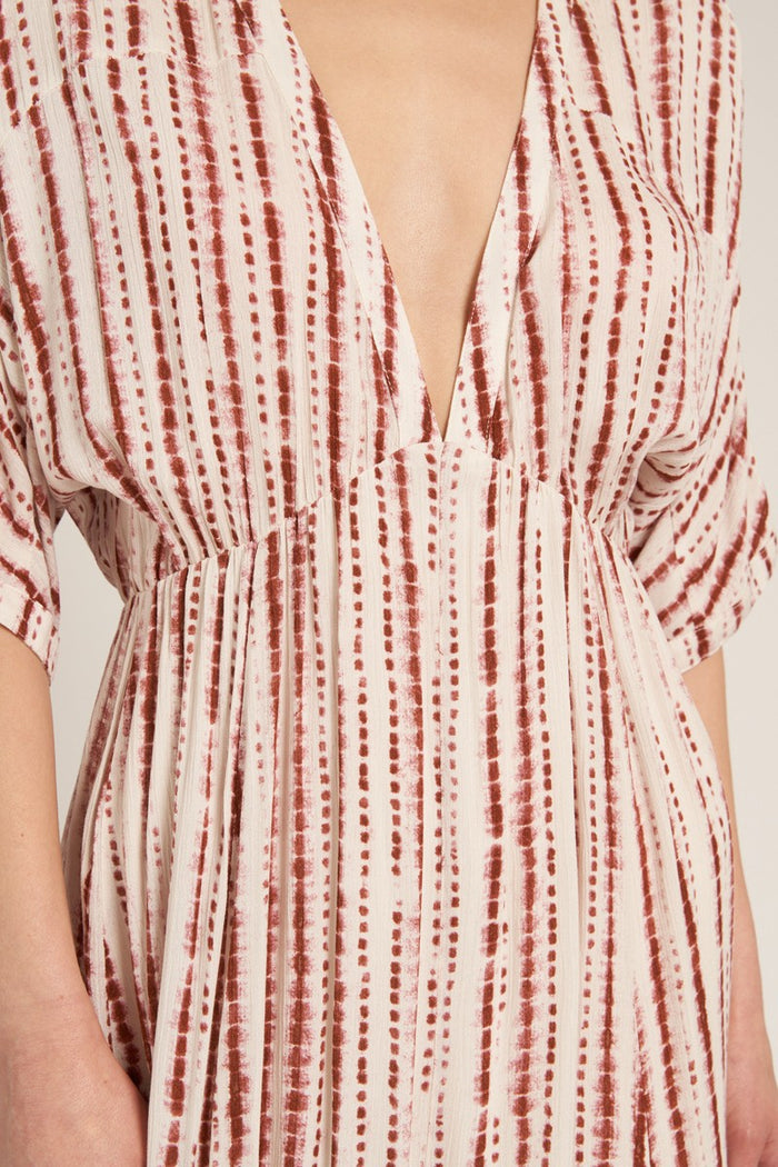 woman wearing a patterned deep v-neck midi dress with short sleeves and flowing fabric in shades of cream and rust