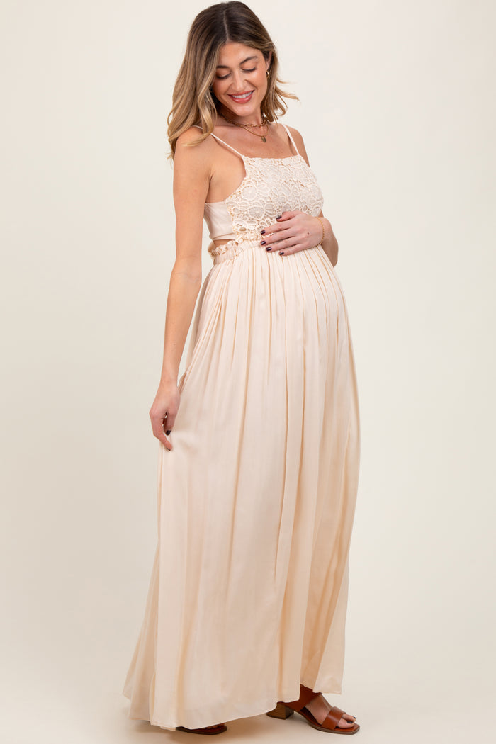 woman wearing a light peach maternity maxi dress with lace detailing, gently cradling her baby bump