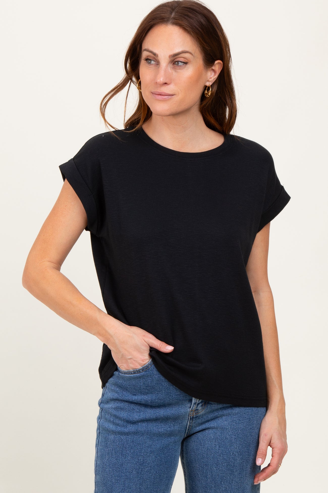 woman wearing a black short sleeve top with rolled cuffs and front pocket, paired with blue jeans