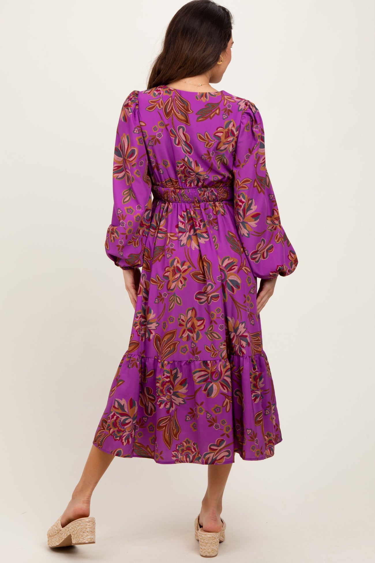 woman wearing a purple floral midi dress with long sleeves and a tiered skirt, styled with a cinched waist