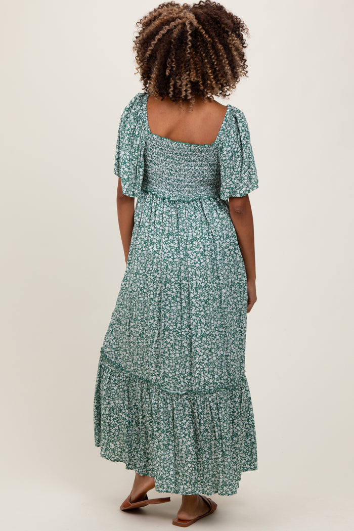 woman wearing a green floral maternity maxi dress with flutter sleeves and a tiered skirt, showing her back