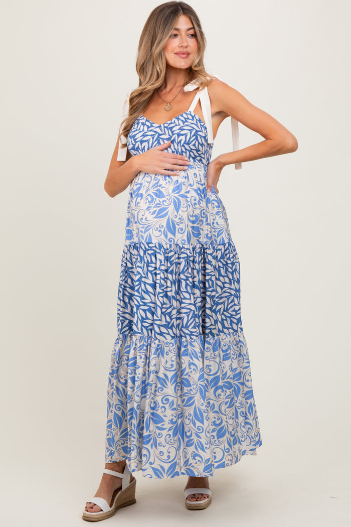 woman wearing a blue and white floral maternity maxi dress with tie straps and holding her baby bump