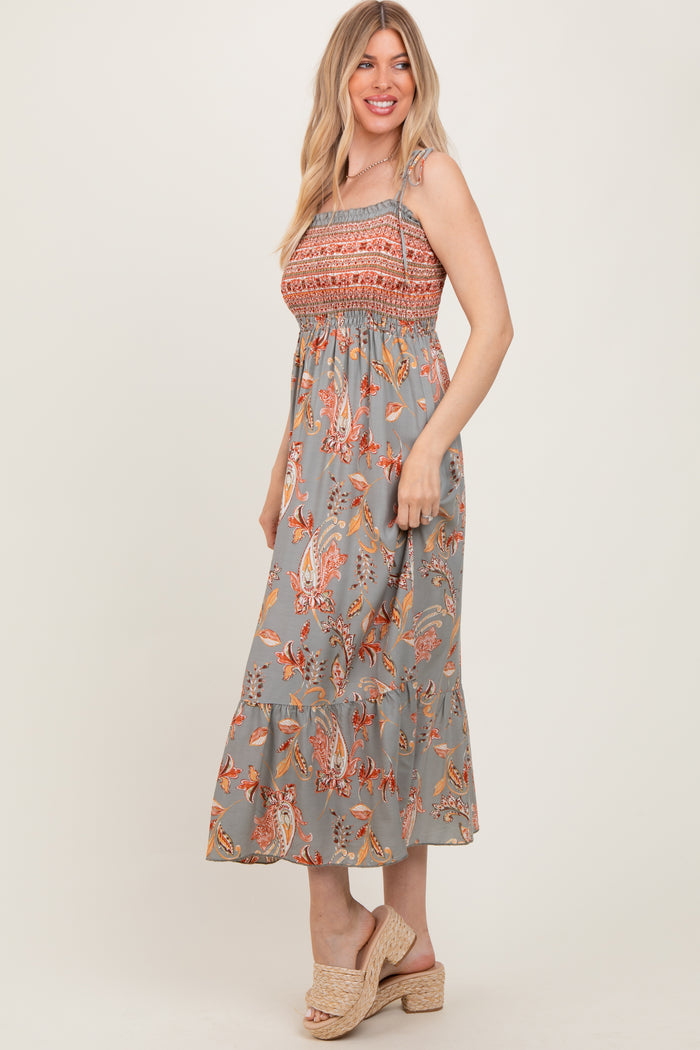woman wearing a gray floral smocked maxi dress with ruffled hem and strappy details, standing sideways