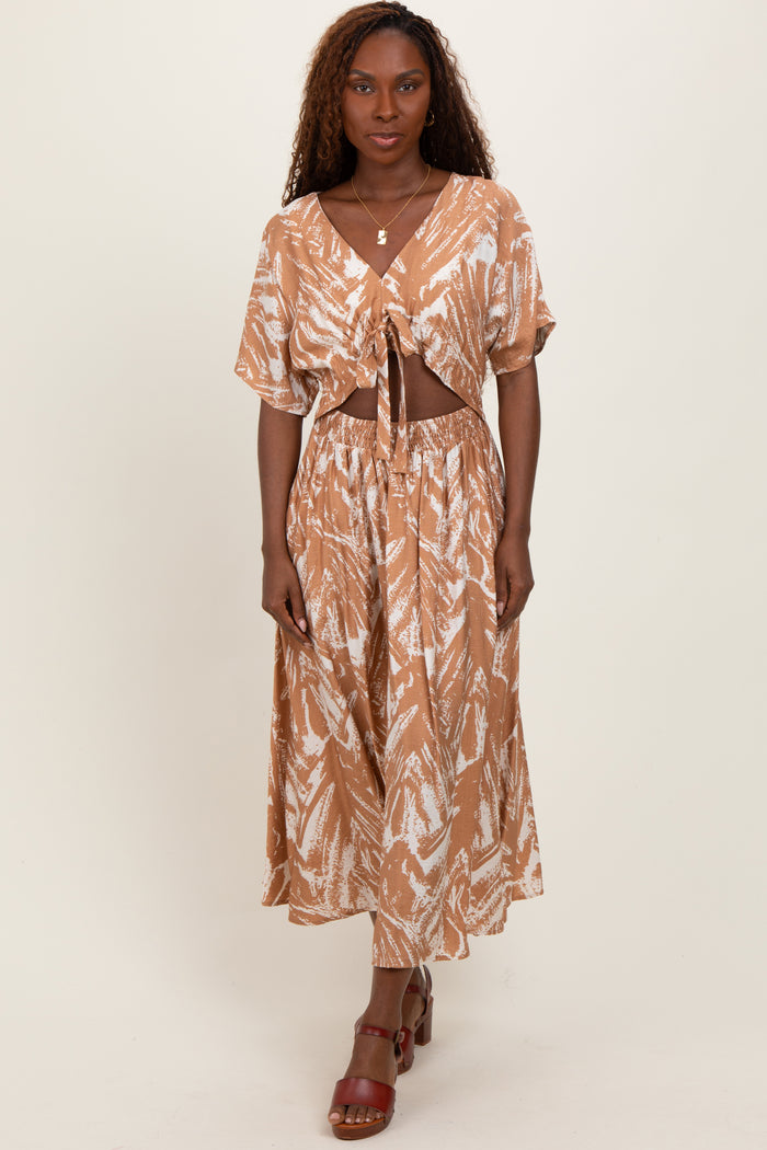 woman wearing a brown tie-front cropped top and matching maxi skirt with a leaf print and high slit