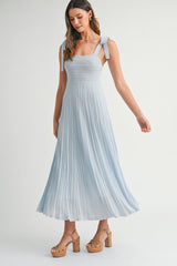 woman wearing a light blue pleated maxi dress with adjustable tie straps and platform wedge heels