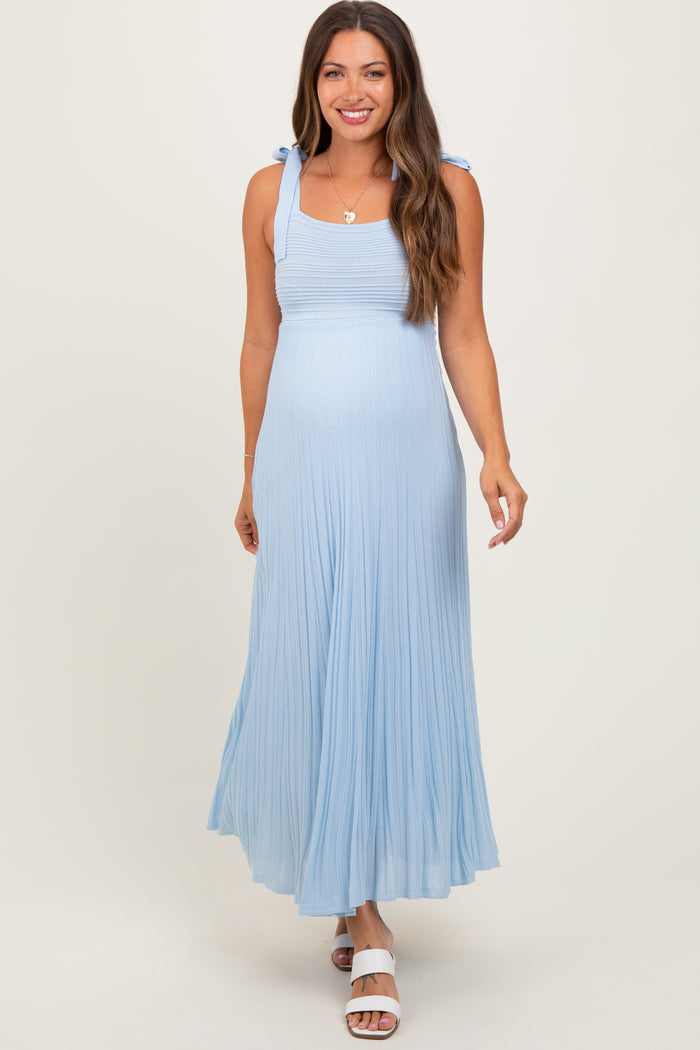 woman wearing a light blue maternity maxi dress with tie strap details and flowing pleats