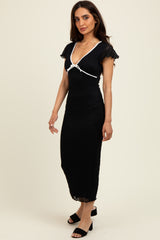 woman wearing a black midi dress with cap sleeves and a white ribbon detail, standing against a light background