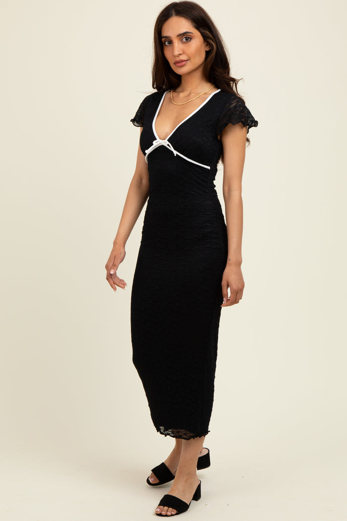 woman wearing a black midi dress with cap sleeves and a white ribbon detail, standing against a light background