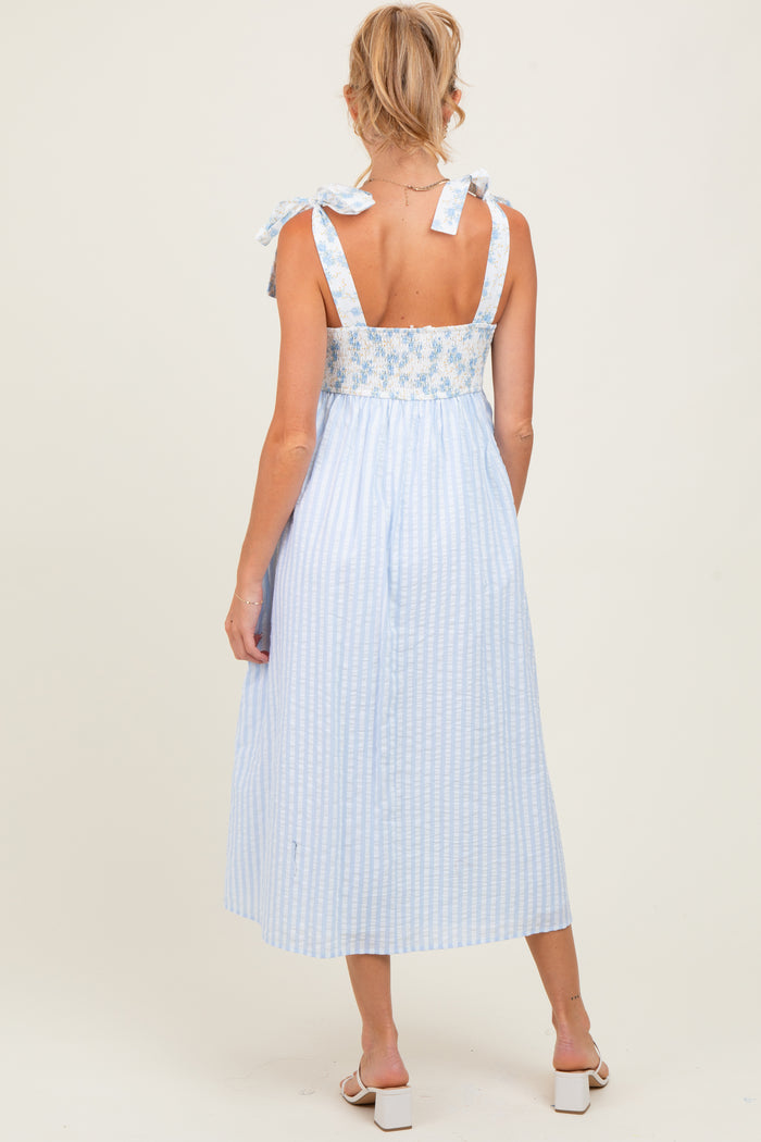 woman wearing a light blue maternity dress with floral details and tie straps, showing a relaxed fit and mid-length style