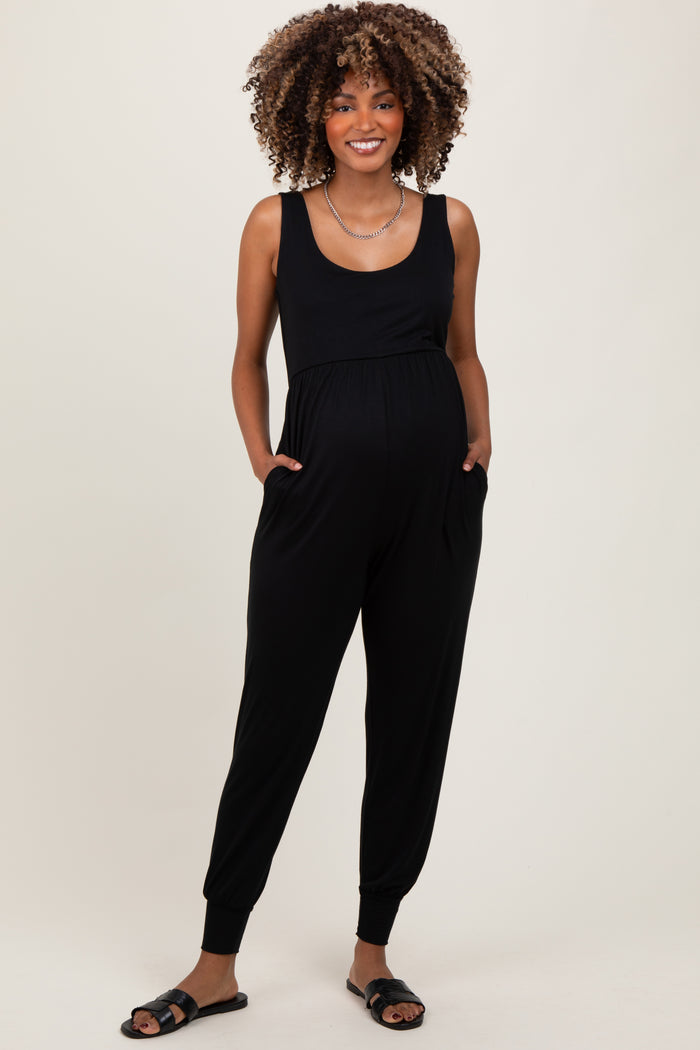 woman wearing a black maternity jumpsuit with a scoop neckline and side pockets, showing her baby bump