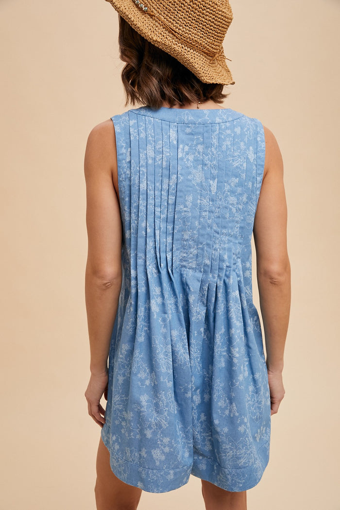 woman wearing a light blue sleeveless dress with back pleats and floral pattern, turned away from the camera